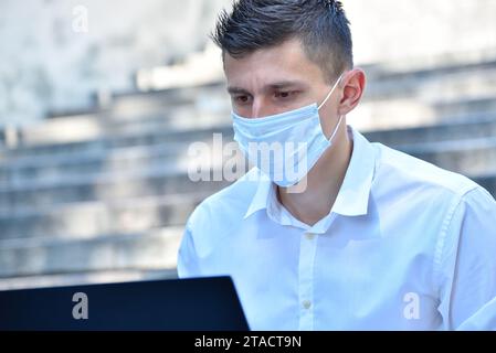 Young businessman in mask working outdoor on laptop computer. Pandemia and coronavirus concept Stock Photo
