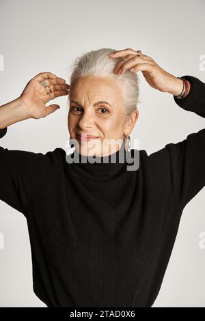 portrait of happy middle aged business woman in elegant attire and hoop earrings adjusting grey hair Stock Photo