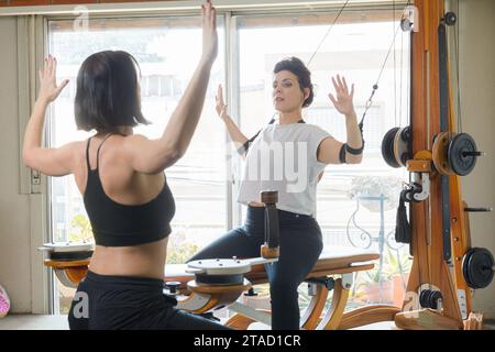 female instructor and student are sitting on exercise machine at home, working together, doing rehabilitation exercises. Stock Photo