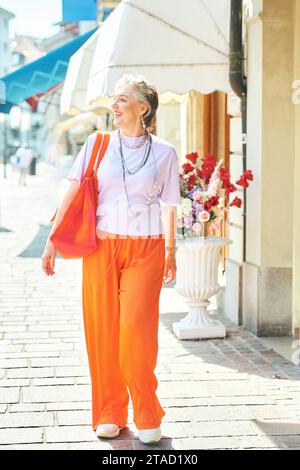 Outdoor fashion portrait of stylish mature 50 - 55 year old woman with grey hair walking down the street Stock Photo