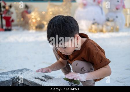Little Asian boy playing in artificial snow during Christmas festival Stock Photo