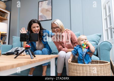 Mother baby and grandmother talking on video call on smart phone in the living room with baby's father. Stock Photo