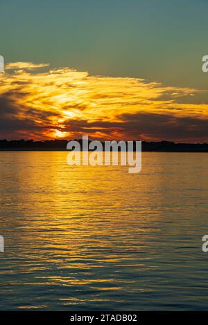 Clouds hide setting sun giving golden glow across the calm Mississippi River in Missouri Stock Photo