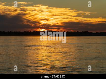 Clouds hide setting sun giving golden glow across the calm Mississippi River in Missouri Stock Photo