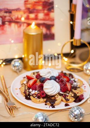 Viennese waffles with berries on a wooden table, breakfast, no people. Festive dessert, candles and string lights on the background Stock Photo