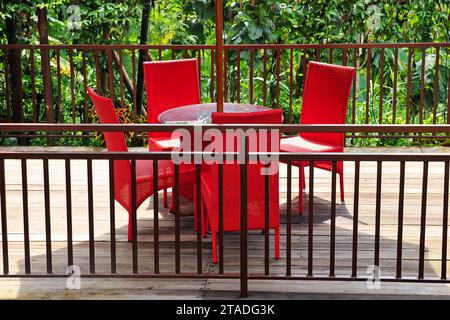 Garden gazebo with a glass table and red woven chairs with a trellis fence and umbrella Stock Photo