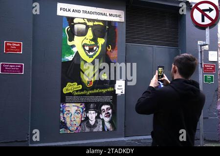 A man photographs an image of Shane MacGowan, lead singer of The Pogues, on a building in the Temple area of Dublin. Shane MacGowan has died aged 65, his wife has announced in a post on Instagram. Picture date: Thursday November 30, 2023. Stock Photo