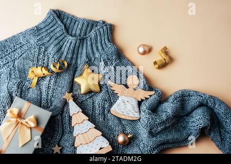 Christmas gifts and baubles on grey sweater on beige background. Top view, flat lay. Stock Photo