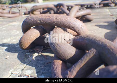 An aged metal chain, its once gleaming surface is now rusty, lies draped upon a weathered concrete floor. Its heavy links bear the passage of time. Stock Photo