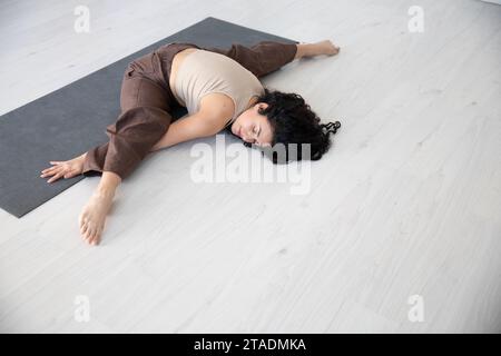 Beautiful sporty curly woman doing yoga asana fitness exercises on the floor Stock Photo