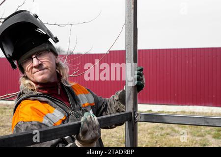 A welder installs an iron frame for construction. Welding metal profiles. Stock Photo