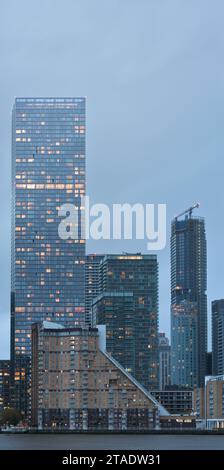 Landmark Pinnacle behind Cascades Tower, river Thames waterside apartments, amongst other buildings at Canary Wharf, London, England, lit up at dusk. Stock Photo