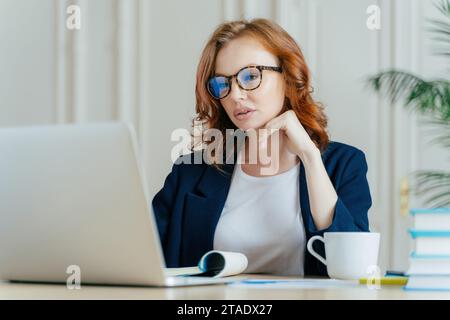 Focused businesswoman with laptop, contemplating in a well-lit office space Stock Photo