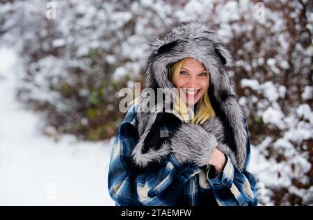 Winter fashion. Beautiful woman in warm clothing in winter park. Female stylish model walking in winter nature. Smiling girl in plaid coat, fur hat Stock Photo