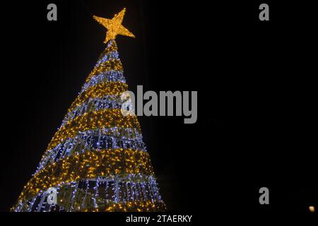 Ground view image of a Christmas tree decorated with stars and LED lights with a dark background and copy space on the right Stock Photo