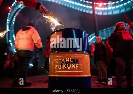 Duisburg, Germany. 30th Nov, 2023. A torch is thrown into a barrel bearing the slogan 'Steel is the future' during a demonstration. Trade unionists from the Duisburg steel companies and delegations from surrounding branches symbolically heralded the end of the peace obligation. The trade unionists made a torchlight march from the Hüttenschenke of Hüttenwerke Krupp Mannesmann to the viewing platform at the Tiger & Turtle in Duisburg. Credit: Fabian Strauch/dpa/Alamy Live News Stock Photo