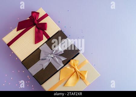 Three gift boxes on purple background with confetti. Christmas, New Year or birthday concept. Top view, flat lay, copy space. Stock Photo