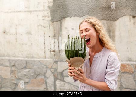 Angry woman holds plant in front of her face and screaming at it Stock Photo