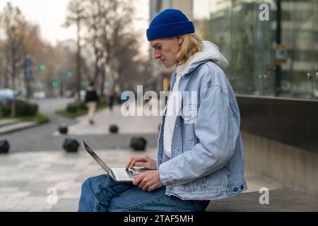 Concentrated self-sufficient man with laptop sits near building works as programmer in IT company Stock Photo