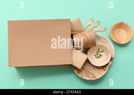 Paper bag with disposable eco tableware on turquoise background Stock Photo