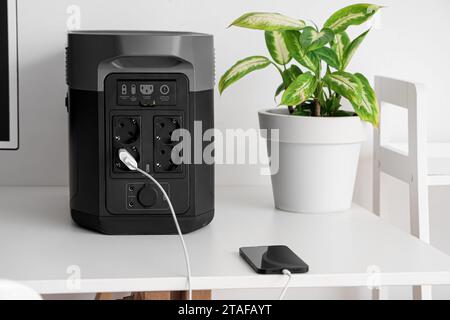 Mobile phone charging from portable power station on white table, closeup Stock Photo