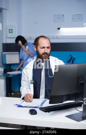 Selective focus on a white doctor studying a patient X-ray chest picture, and writing on his notepad. Close-up of a man with a lab coat, holding and examining a patient's chest scan. Stock Photo
