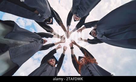 Team of college or university students celebrating graduation. Group of happy successful graduates in academic hats and robes standing in circle and Stock Photo