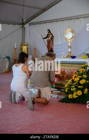 A middle-aged couple kneeling in adoration of the Blessed Sacrament. A tent at the Sanctuary of Christ the King in Lisbon, Portugal during WYD 2023. Stock Photo