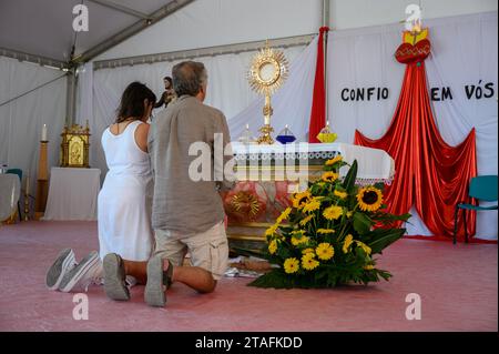 A middle-aged couple kneeling in adoration of the Blessed Sacrament. A tent at the Sanctuary of Christ the King in Lisbon, Portugal during WYD 2023. Stock Photo