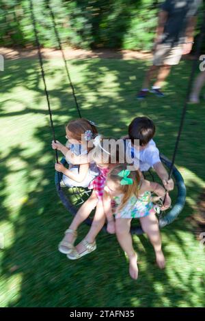 Group of kids ride together on a round rope swing in the backyard, Miami, Florida, USA Stock Photo