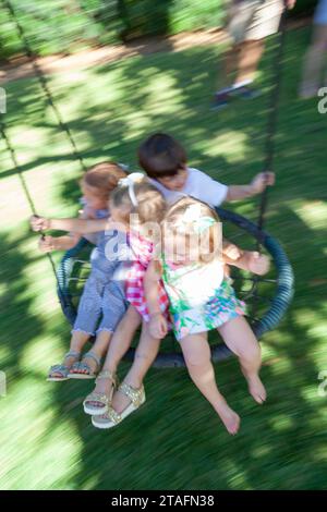Group of kids ride together on a round rope swing in the backyard, Miami, Florida, USA Stock Photo