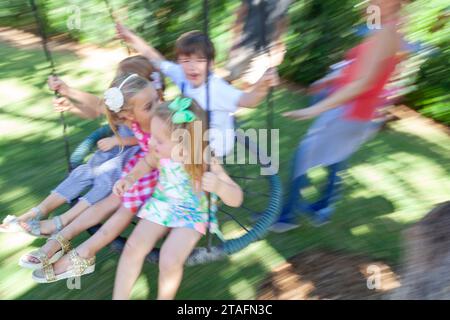 Group of kids ride together on a round rope swing in the backyard, Miami, Florida, USA Stock Photo
