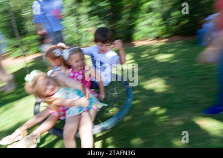 Group of kids ride together on a round rope swing in the backyard, Miami, Florida, USA Stock Photo