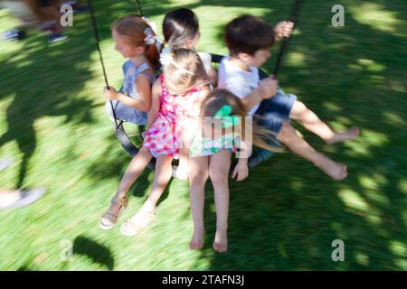 Group of kids ride together on a round rope swing in the backyard, Miami, Florida, USA Stock Photo