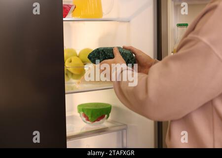 Man putting bowl covered with beeswax food wrap into refrigerator, closeup Stock Photo