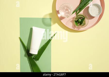 The white lotion tube is displayed with aloe vera. A glass of water, a bowl of salt and a glass containing sliced aloe vera are placed together on a p Stock Photo
