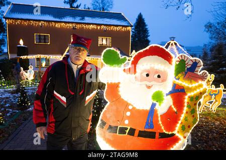 PRODUCTION - 27 November 2023, Saxony, Großröhrsdorf: Rüdiger Browatzke stands in front of his festively decorated property. For more than 20 years, the 68-year-old has been decorating his house and garden with festive decorations and Christmas lights. Photo: Sebastian Kahnert/dpa Stock Photo