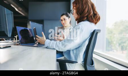 Female colleagues actively collaborate in a modern office, engaging in discussions, coding and programming. Skilled women creating innovative software Stock Photo