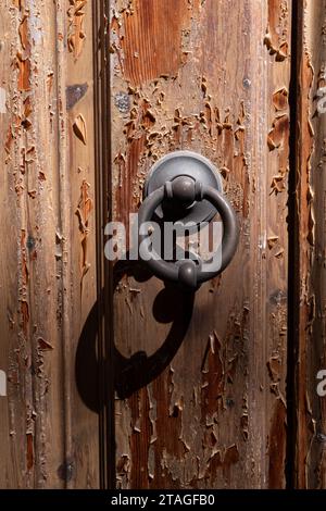 A small, round, metal knocker is mounted to an old Italian door with peeling paint in Tuscany, Italy. Stock Photo