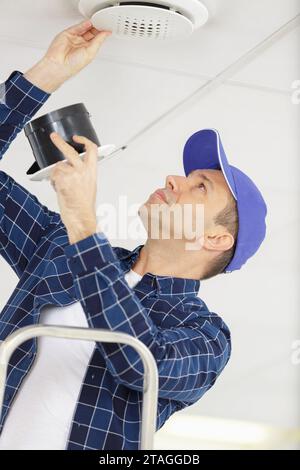 young electrician installing fire alarm unit on ceiling Stock Photo