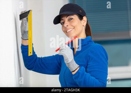 female builder holding a set square against the wall Stock Photo