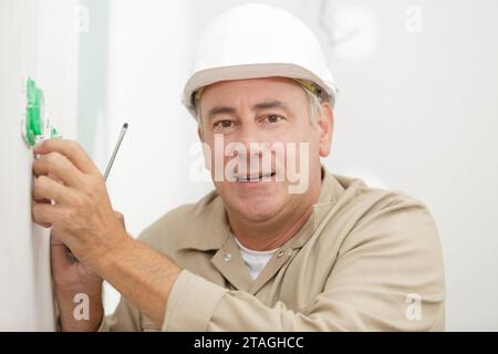 a mature electrician installing socket Stock Photo