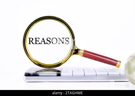 REASONS lettering through a magnifying glass on a calculator and part of a magic ball in the foreground without focus Stock Photo