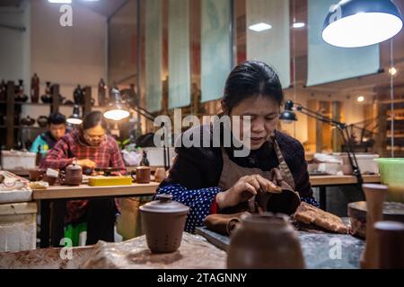 (231201) -- CHONGQING, Dec. 1, 2023 (Xinhua) -- People work at Liang Xiancai's studio in Rongchang District of Chongqing, southwest China, Nov. 14, 2023.  Liang Xiancai, 73, is an inheritor of Rongchang Pottery craftsmanship, an intangible cultural heritage in China. Despite the trend toward mechanization, automation, and large-scale pottery production, he steadfastly upholds the tradition of manual pottery making.   Guan Yongshuang, 32, graduated from the Sichuan Fine Arts Institute with a major in pottery art. He has been studying pottery culture for nearly ten years.   Guan is working on tu Stock Photo