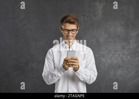Focused cheerful guy uses modern mobile phone to communicate online and browse web. Stock Photo