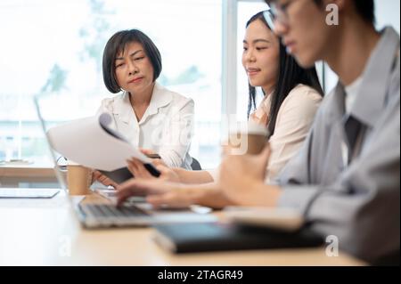 A professional and experienced senior Asian female boss is in the meeting with her team, discussing and brainstorming on a new project together. Stock Photo