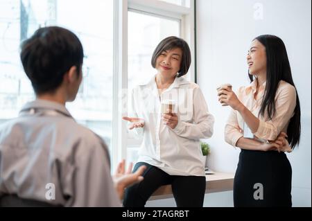 Group of happy diverse Asian businesspeople colleagues are enjoying talking, laughing, and sharing their ideas during a coffee break in the office. Stock Photo
