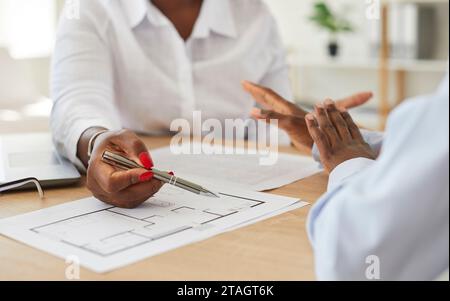 Young interior designer african american woman showing her client floor plan of new house. Stock Photo