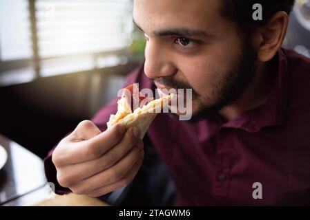 Pizza time concept. Positive male african  office worker or entrpreneur in suit eating big piece of pizza Stock Photo