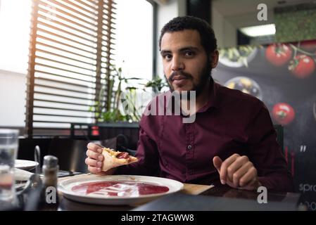 Pizza time concept. Positive male african  office worker or entrpreneur in suit eating big piece of pizza Stock Photo